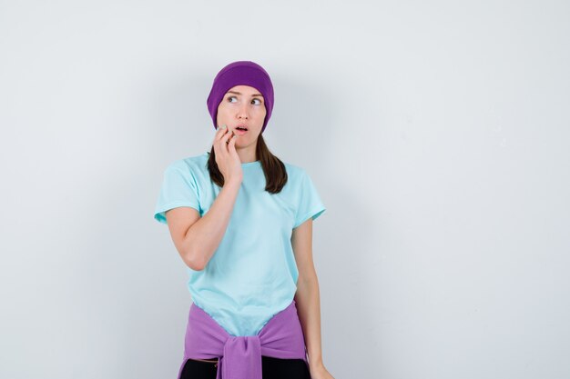 Portrait d'une femme merveilleuse avec la main sur le menton, regardant de côté en chemisier, bonnet et à la vue de face choquée