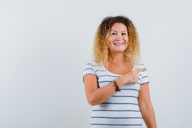 Portrait d'une femme merveilleuse pointant vers le côté droit en t-shirt rayé et regardant la vue de face joyeuse