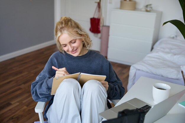 Portrait d'une femme mignonne et souriante blogueuse de style de vie assise dans sa chambre avec un journal quotidien ou un planificateur