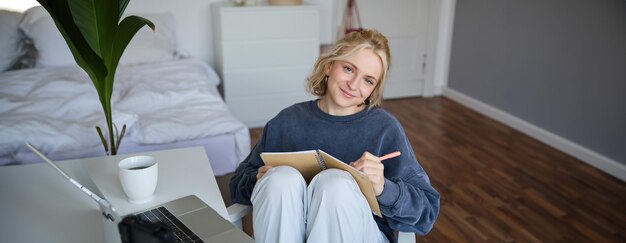 Portrait d'une femme mignonne et souriante blogueuse de style de vie assise dans sa chambre avec un journal quotidien ou un planificateur