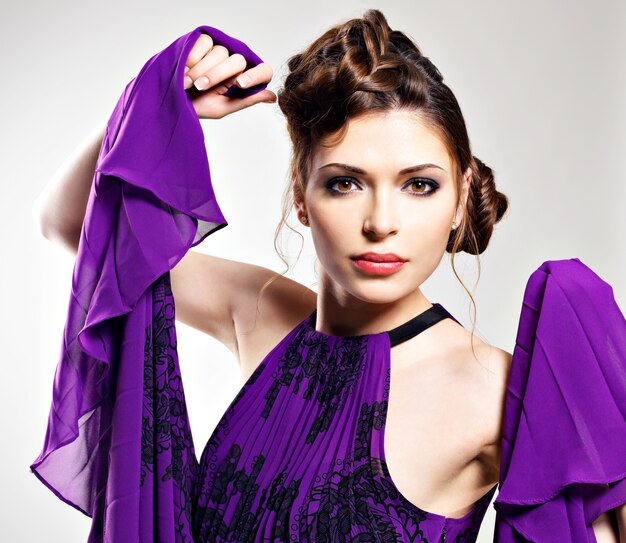 Portrait de la femme de mode en robe violette avec une coiffure élégante pose au studio