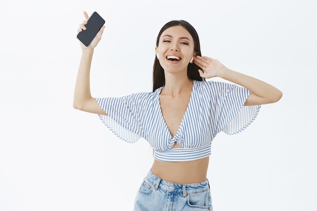 Portrait de femme moderne ravie et amusée insouciante en haut recadrée danse tenant la musique d'écoute de smartphone