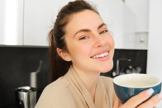 Portrait d'une femme moderne souriante et heureuse commence sa journée avec une tasse de thé du matin, une fille buvant du café