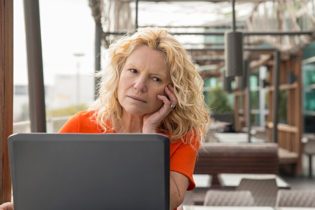 Portrait de femme mûre songeuse travaillant à l&#39;ordinateur portable au café