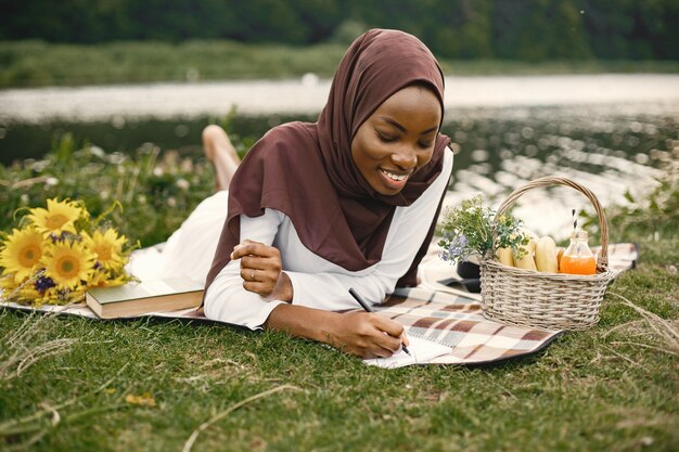 Photo gratuite portrait d'une femme musulmane allongée sur la couverture de pique-nique à carreaux près de la rivière