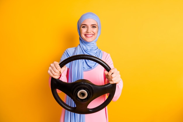 Portrait d'une femme musulmane joyeuse professionnelle au contenu attrayant portant le hijab conduisant une location de voiture invisible isolée sur fond de couleur jaune vif