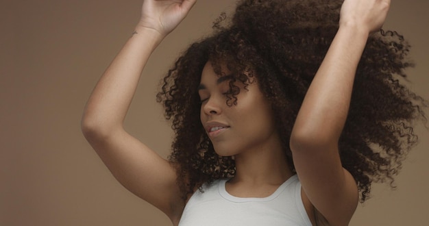 Photo gratuite portrait de femme noire métisse avec de grands cheveux bouclés afro sur fond beige danse agrandi