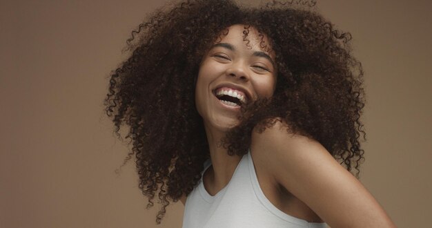 Portrait de femme noire métisse avec de grands cheveux bouclés afro sur fond beige Rire naturel