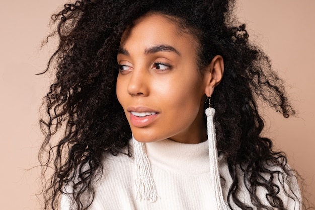 Portrait de femme à la peau foncée avec des cheveux bouclés souriant sur beige