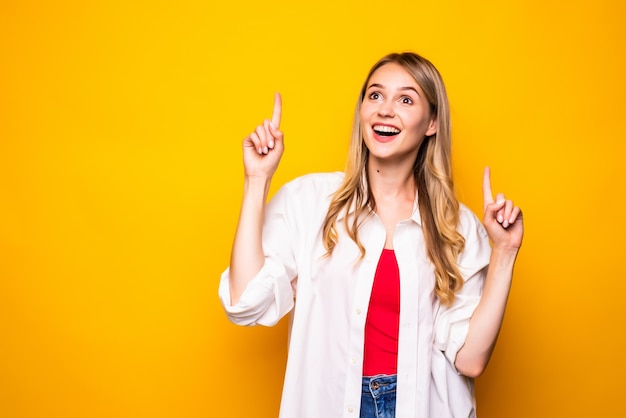 Portrait de femme pointant avec deux doigts et bouche ouverte, isolé sur mur jaune