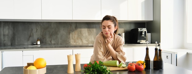 Photo gratuite portrait d'une femme qui pense à ce qu'elle doit cuisiner avec des légumes en regardant une planche à découper avec des tomates avec