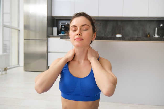 Photo gratuite portrait d'une femme qui s'entraîne à domicile, fait des exercices d'entraînement, étirent le cou, s'échauffent avant de se remettre en forme.