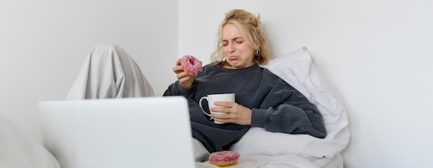 Photo gratuite portrait d'une femme regardant un film triste sur un ordinateur portable en pleurant et en essuyant ses larmes en mangeant des beignets et