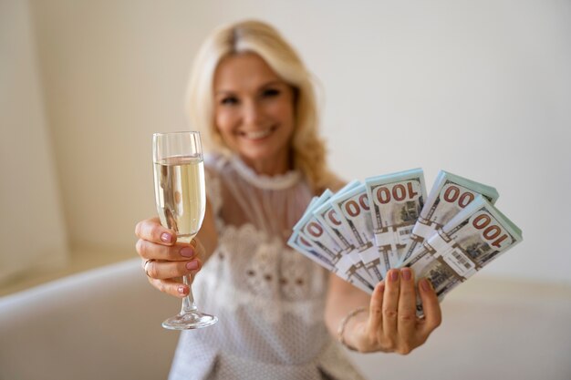 Portrait d'une femme riche blonde d'âge moyen avec un verre de champagne et des billets