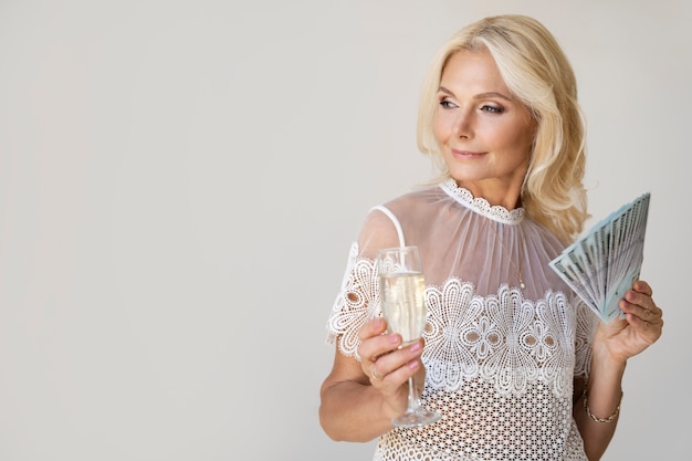 Portrait d'une femme riche blonde d'âge moyen avec un verre de champagne et des billets