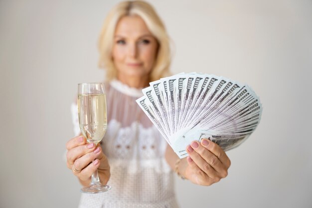 Portrait d'une femme riche blonde d'âge moyen avec un verre de champagne et des billets