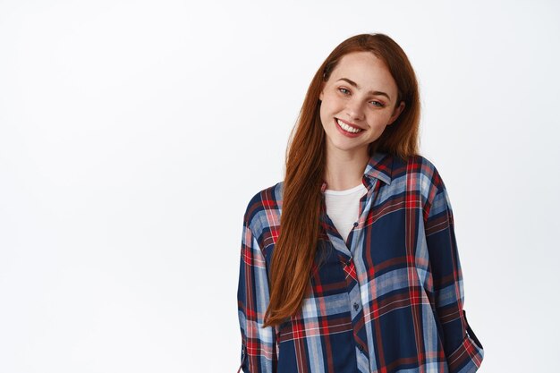 Portrait d'une femme rousse mignonne et tendre avec des taches de rousseur, regardant avec tendresse et douce sensation réconfortante, souriant à la caméra, fond blanc.