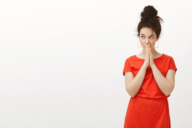 Portrait de femme séduisante troublée intense en jolie robe rouge décontractée, tenant par la main en prière