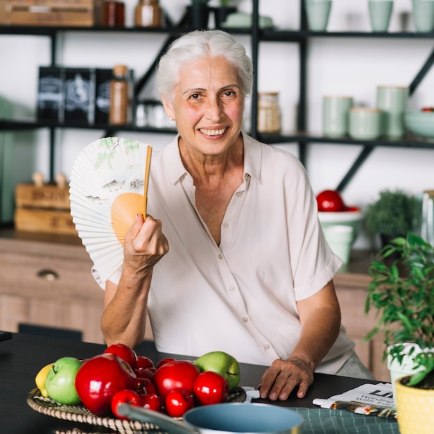 Portrait De Femme Senior Souriante Assise Devant Des Fruits Sur Une Table