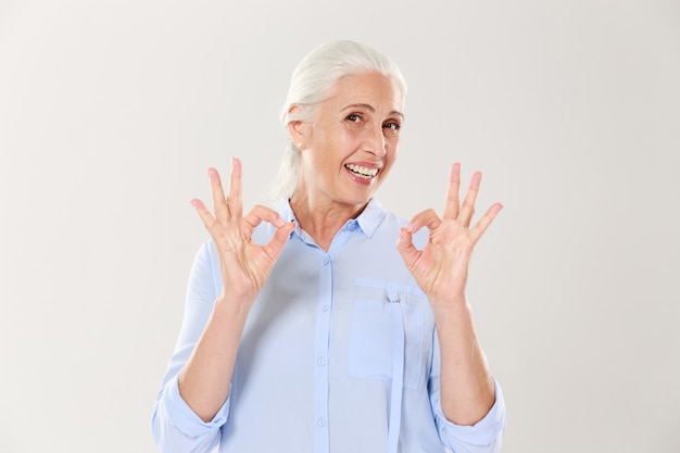 Portrait de femme senior souriante en chemise bleue montrant le geste OK