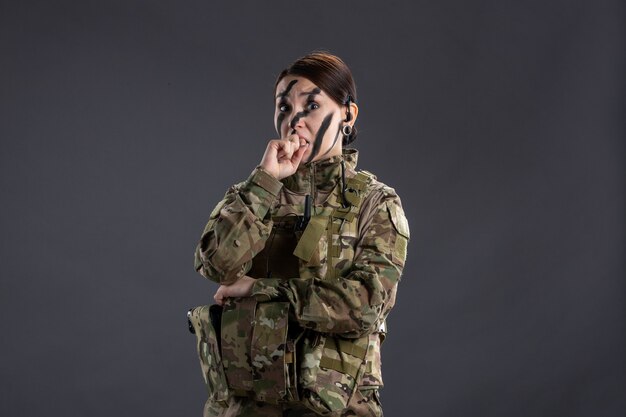 Portrait de femme soldat en camouflage sur le mur sombre