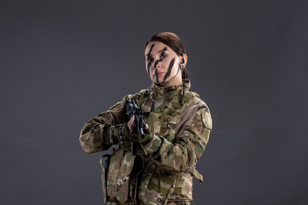 Photo gratuite portrait de femme soldat en tenue de camouflage avec mitrailleuse sur le mur sombre