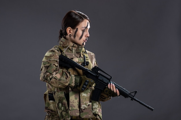 Portrait de femme soldat en tenue de camouflage avec mitrailleuse sur le mur sombre