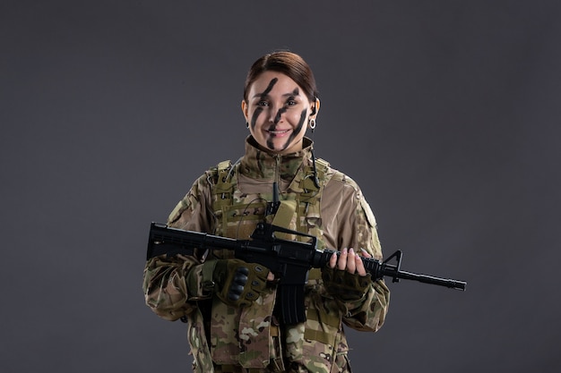 Portrait de femme soldat en tenue de camouflage avec mitrailleuse sur le mur sombre