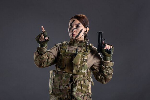 Portrait de femme soldat en tenue de camouflage avec mur sombre pistolet