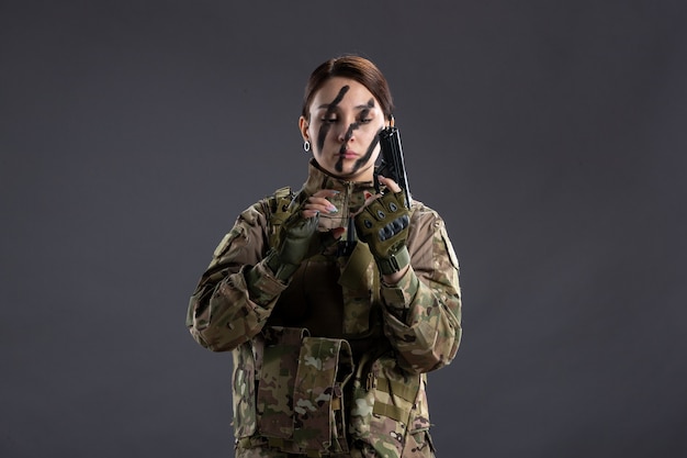 Portrait de femme soldat en tenue de camouflage avec mur sombre pistolet