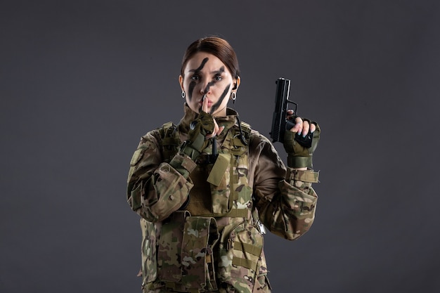 Portrait de femme soldat en tenue de camouflage avec mur sombre pistolet