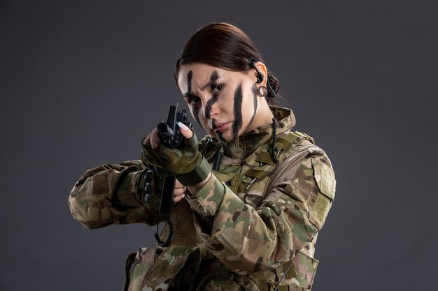 Portrait de femme soldat en uniforme militaire avec mitrailleuse sur le mur sombre