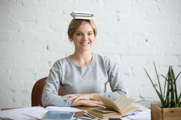 Portrait de femme souriante au bureau, livres sur sa tête