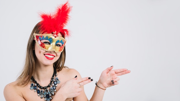 Portrait d&#39;une femme souriante portant masque de carnaval gesticulant sur fond blanc