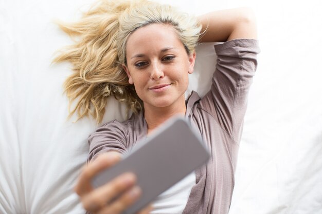 Portrait de femme souriante prenant Selfie au lit