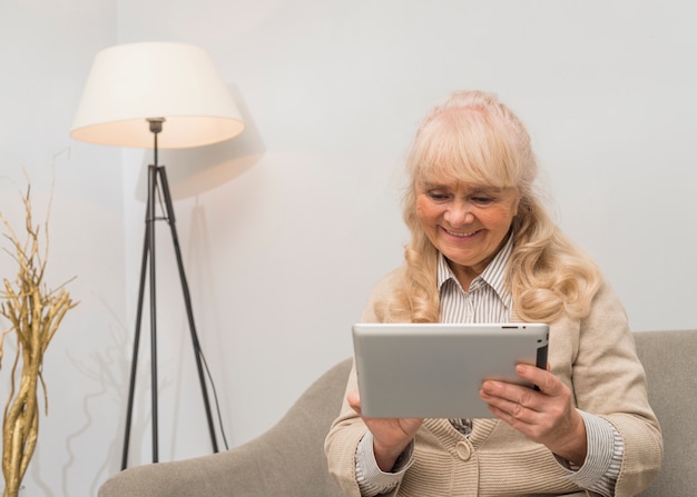 Photo gratuite portrait d'une femme souriante regardant une tablette numérique assise sur un canapé