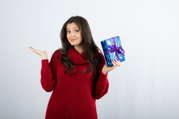 Portrait d'une femme souriante tenant une boîte-cadeau de Noël avec ruban violet.