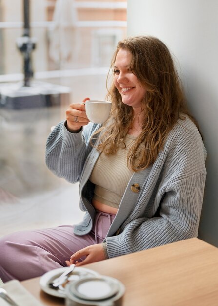 Portrait d'une femme de taille plus en train de boire un verre dans un restaurant