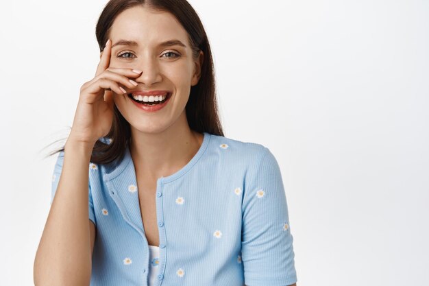 Portrait d'une femme tendre et belle, touchant la peau naturelle du visage avec une lueur saine et un look frais, riant et souriant des dents blanches, regardant la caméra, fond de studio