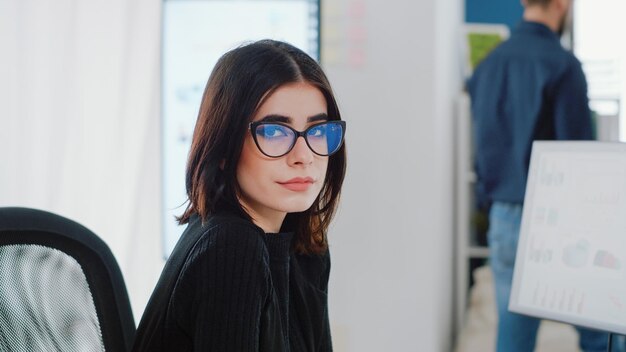 Portrait de femme avec un travail d'affaires assis au bureau. Gros plan sur une femme d'affaires regardant la caméra et souriant tout en utilisant un ordinateur avec des graphiques de débit de données sur le moniteur pour le projet.