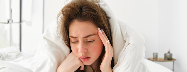 Portrait d'une femme triste se sentant mal au lit sous une couverture blanche touchant la tête a mal à la tête