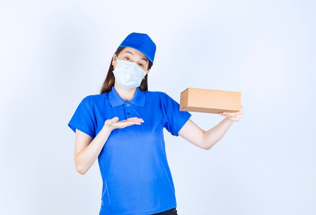 Portrait de femme en uniforme et masque médical tenant une boîte en papier