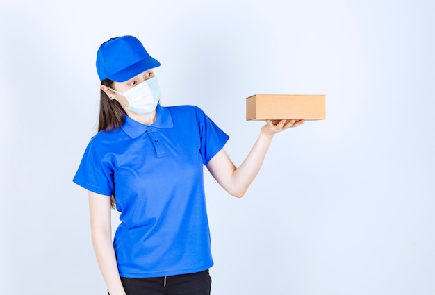 Portrait de femme en uniforme et masque médical tenant une boîte en papier