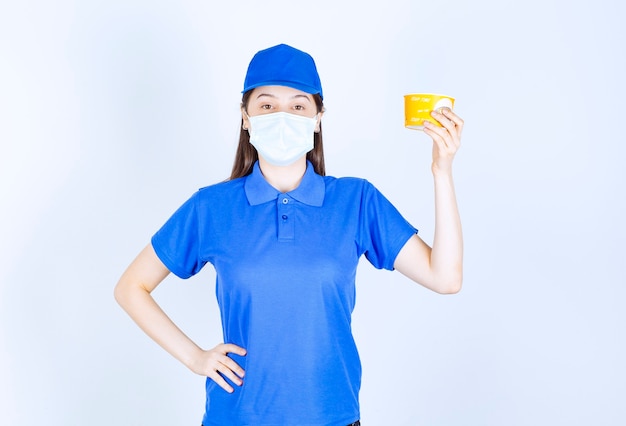 Portrait de femme en uniforme et masque médical tenant une tasse en plastique