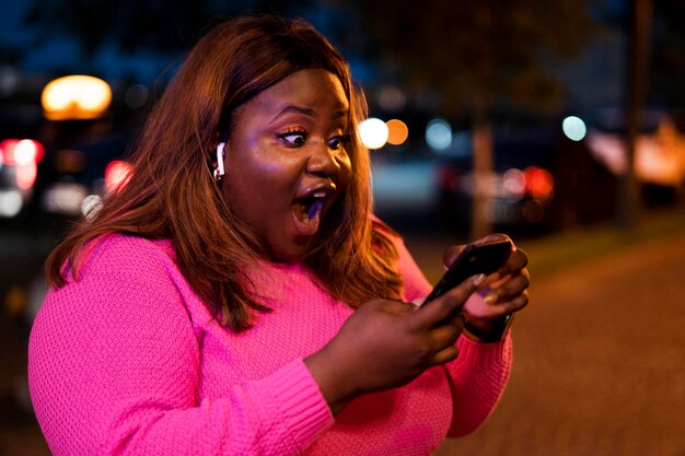 Portrait de femme utilisant un smartphone la nuit dans les lumières de la ville