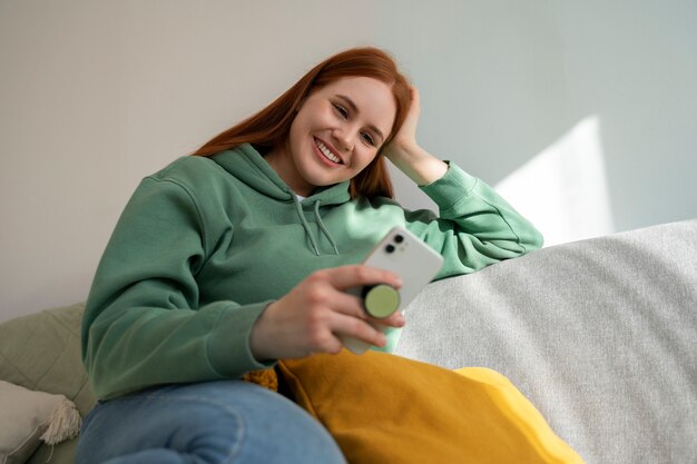 Portrait d'une femme utilisant son smartphone à la maison sur un canapé en se tenant à partir d'une prise pop