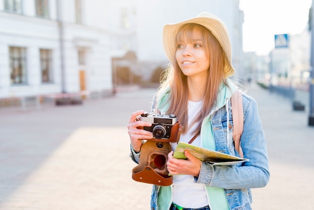 Photo gratuite portrait, femme, voyageur, ville, tenue, appareil photo vintage, carte, main, regarder, loin