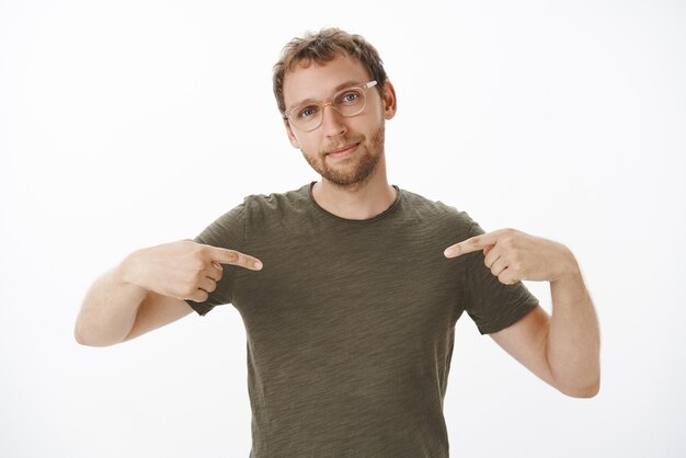 Portrait de fier et heureux entrepreneur masculin beau à lunettes et t-shirt vert foncé pointant sur lui-même et souriant se vantant de ses propres réalisations