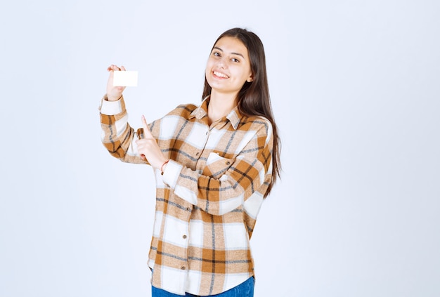 Portrait d'une fille adorable avec une carte de visite vierge debout sur un mur blanc.