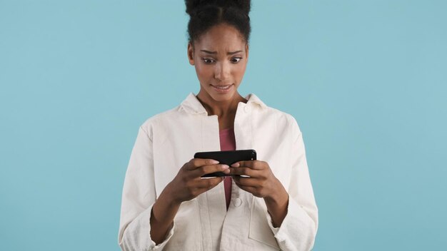 Portrait d'une fille afro-américaine décontractée choquée regardant une vidéo sur un smartphone avec émerveillement sur fond coloré